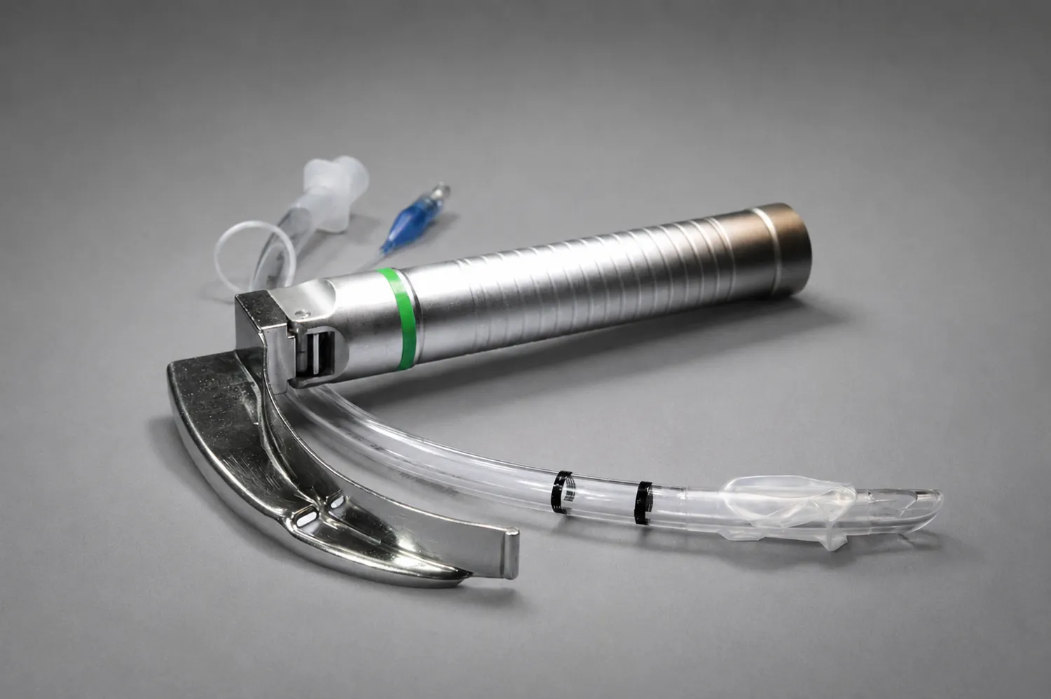 Hahn – Anästhesie Praxis – Ein medizinisches Laryngoskop mit Metallgriff und -spatel neben einem durchsichtigen Endotrachealtubus mit blauem Cuff und einer Spritze.